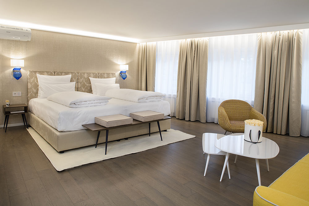 Das Schlafzimmer der Hotelsuite im hellen gold-beigen Design, großen Möbelstücken und viel Freifläche