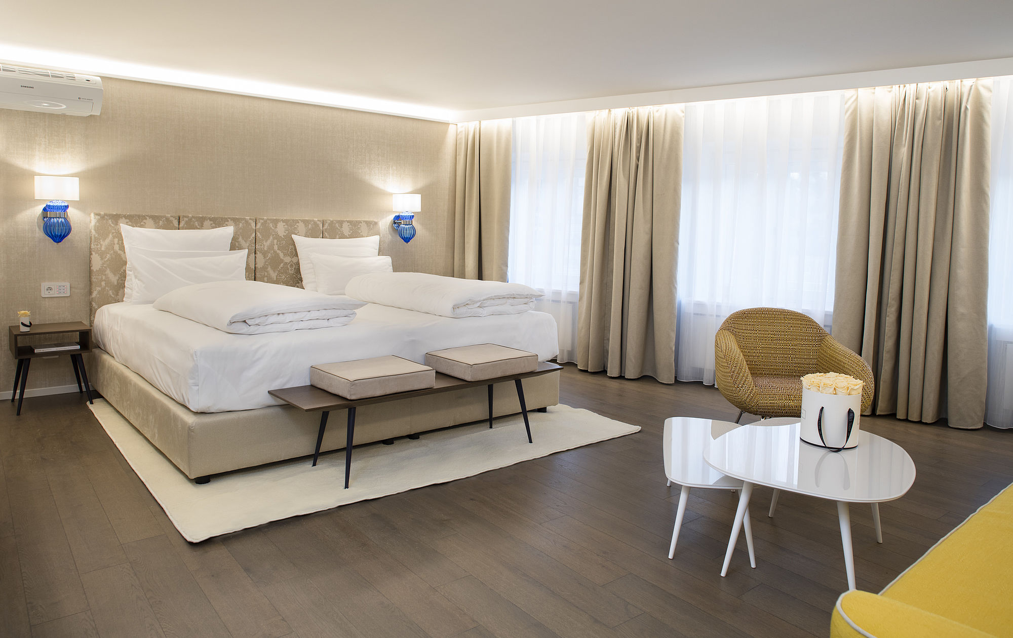 The bedroom of the hotel suite in a light gold-beige design, large pieces of furniture and lots of open space