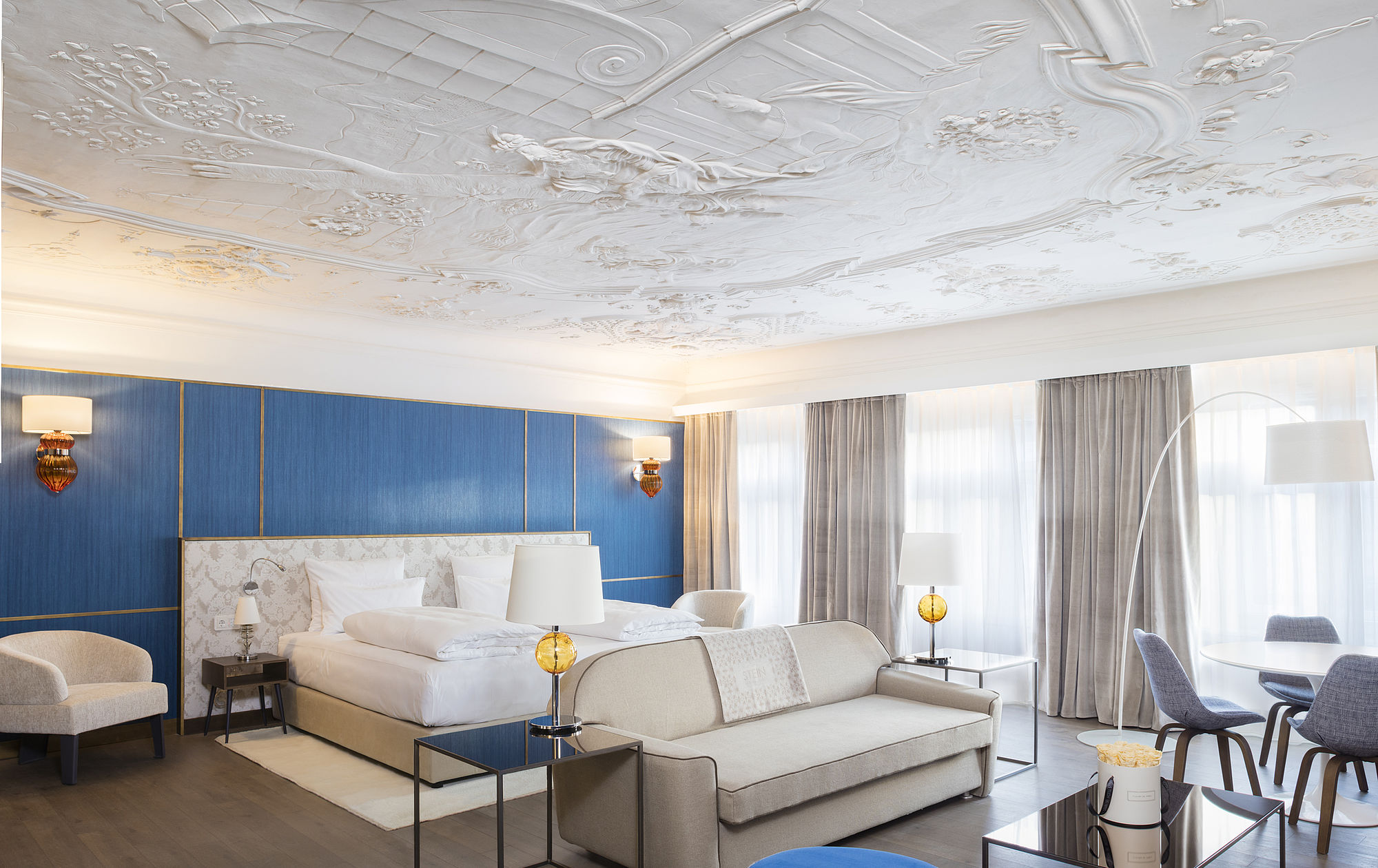 Geräumige, lichtdurchflutete Honeymoon Suite des 4 Sterne Hotels in Salzburg mit historischer Stuckdecke, hellen Möbeln und viel freier Fläche